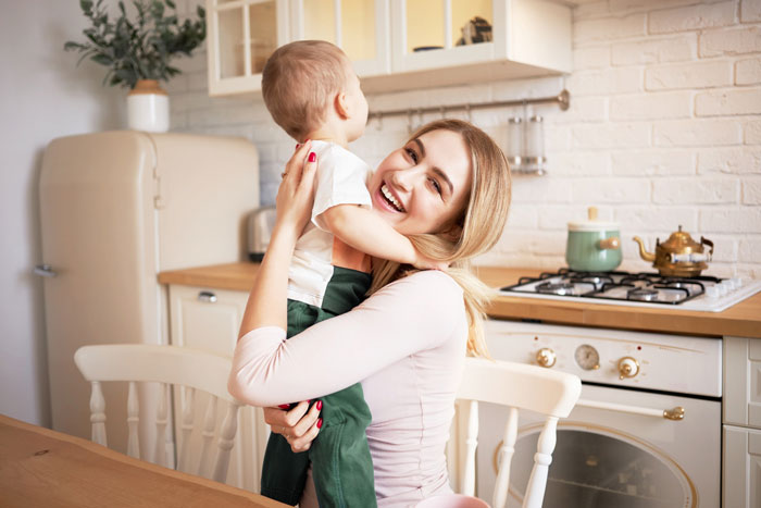 Wife holding toddler in kitchen, showing emotional comfort and responding with same effort in a loving moment. Wife holding toddler in kitchen, showing emotional comfort and responding with same effort in a loving moment.