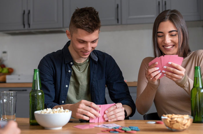 Young man and woman playing cards together, smiling and sharing a casual moment with husband best friend cheating tension.
