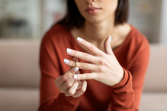Woman in orange shirt removing wedding ring, symbolizing marriage breakup and uncovering gym affair issue.
