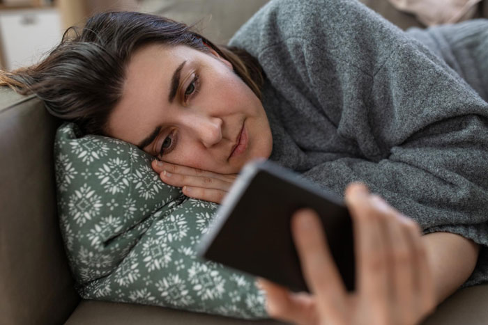 Woman lying on couch looking upset while holding phone, reflecting emotions related to infertile wife’s reaction to baby-making plan.