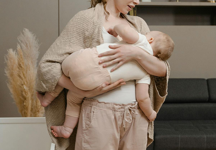 Woman holding and breastfeeding baby indoors in a cozy living room, showing care and nurturing.