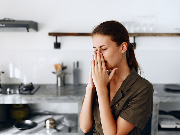 Woman in kitchen upset, covering face with hands, expressing distress and emotions related to divorce papers.