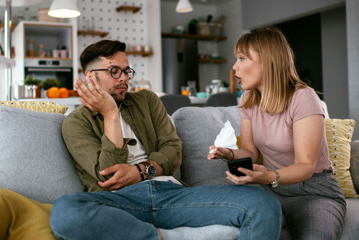 Couple sitting on couch during a tense conversation, illustrating husband lack consideration thoughtfulness in a home setting. Couple sitting on couch during a tense conversation, illustrating husband lack consideration thoughtfulness in a home setting.