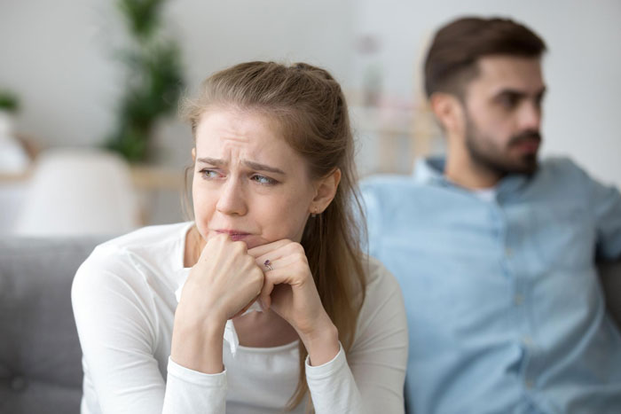 Worried woman looking away while husband shows lack of consideration and thoughtfulness, sitting apart on couch. Worried woman looking away while husband shows lack of consideration and thoughtfulness, sitting apart on couch.