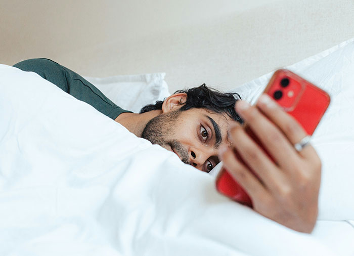 Man lying in bed looking at a red smartphone, reflecting the struggles of a woman with a husband repeatedly leaving and returning.