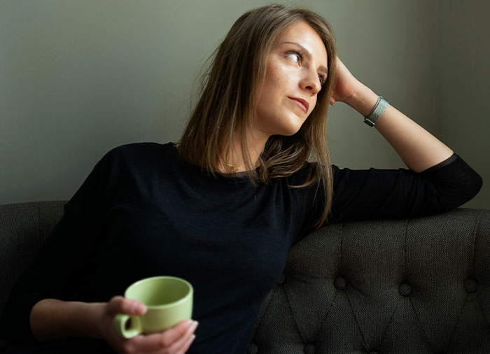 Woman sitting on couch holding a cup, looking pensive, illustrating struggles with husband leaving and coming back.