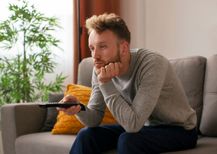 Man sitting on couch with remote control, appearing bossy and indifferent, representing a bossy man locking pregnant wife out.