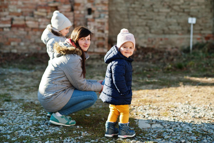 Pregnant woman and children outdoors in freezing weather, woman wearing winter coat and children dressed warmly.