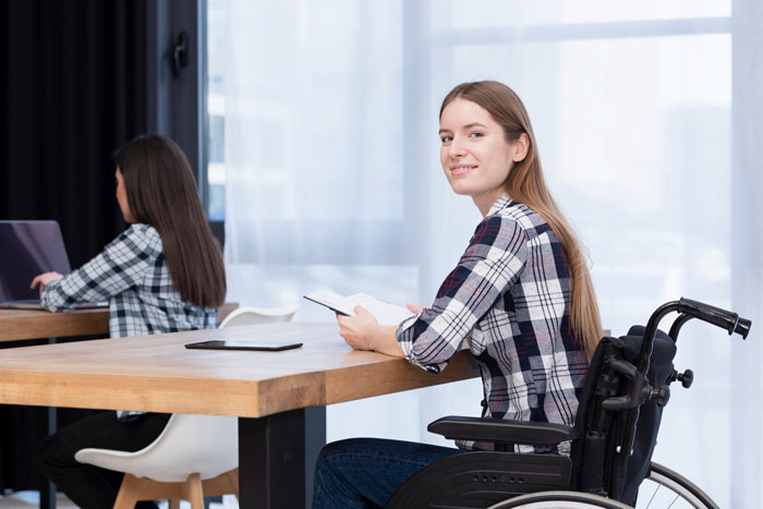 Teen girl in a wheelchair smiling at a desk with another student, highlighting love and wheelchair user concerns.