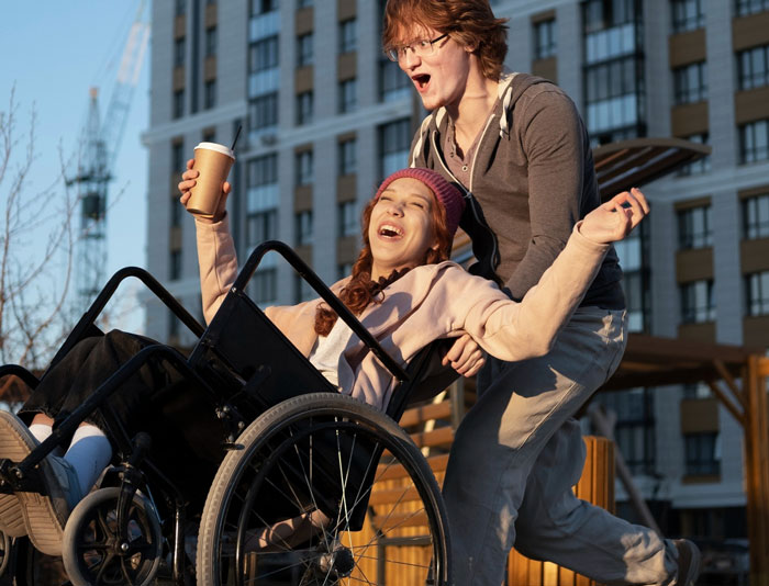 Teen boy happily pushing a wheelchair user outside, highlighting concerns about ableist dad and son's future love life.