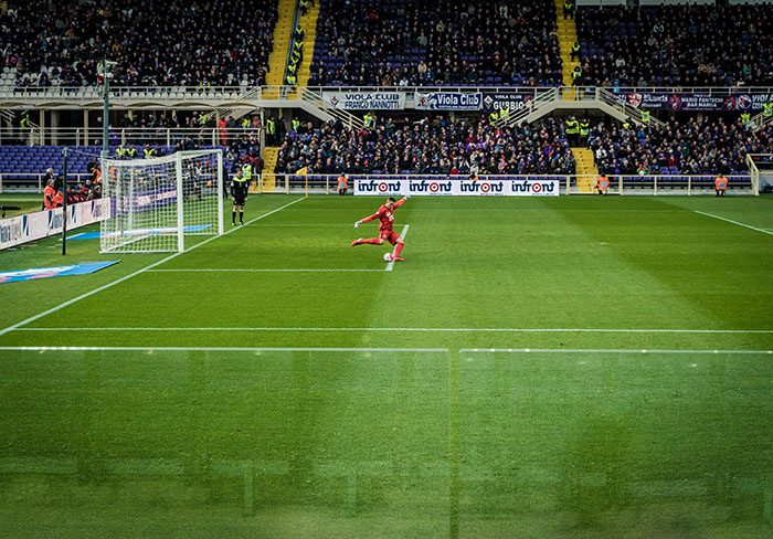 Soccer player in red kicking ball during a match with crowd watching, illustrating spouse draining emergency fund for World Cup.