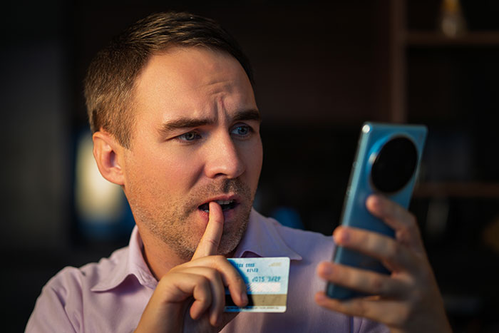 Man holding credit card and smartphone, looking worried as emergency fund drains watching World Cup essentials online.