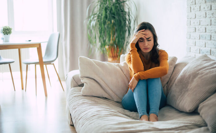 Wife hurt and upset about husband&rsquo;s reaction to her wedding look sitting alone on couch in living room.