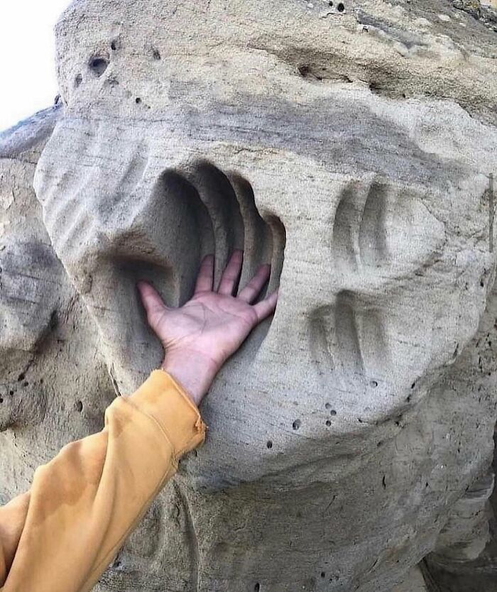 Hand placed inside a perfect hand-shaped rock formation creating a reality glitched illusion with natural textures.