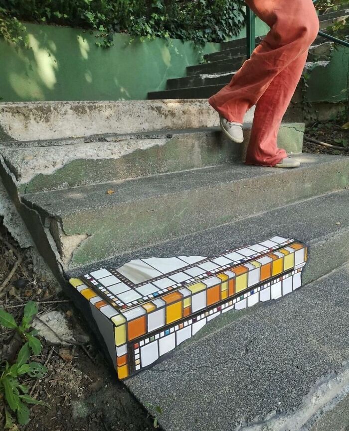Broken outdoor concrete stairs with one step cleverly restored using colorful reality glitch illusion mosaic tiles.