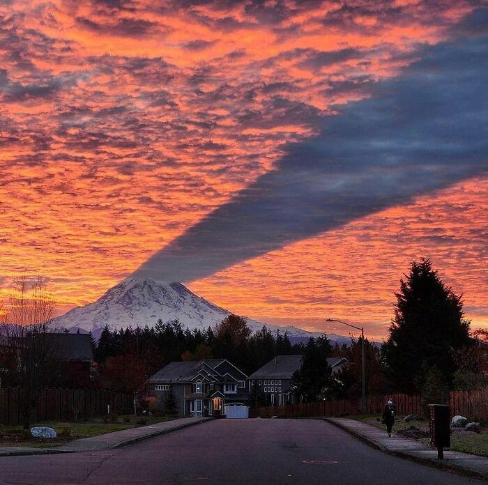 Sunset sky over snowy mountain casting a striking shadow, creating a reality glitched effect in a suburban neighborhood.