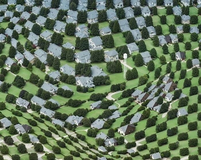 Aerial view of a suburban neighborhood with patterned rows of houses and trees creating a reality glitch illusion.