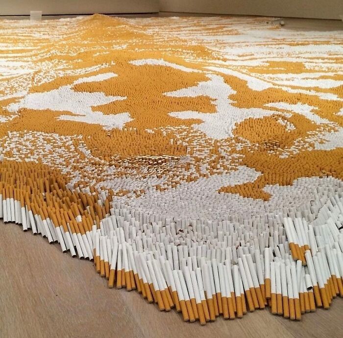 Cleverly staged illusion of a large pixelated image made entirely from arranged cigarettes on a floor.