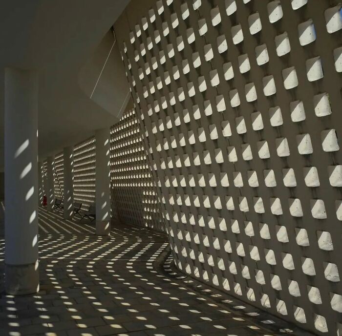Geometric shadows cast by a perforated wall creating a reality glitch effect in a cleverly timed photo illusion.