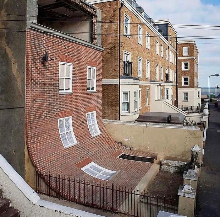 Brick building facade curving unnaturally, creating a reality glitch effect in a perfectly timed illusion photo.