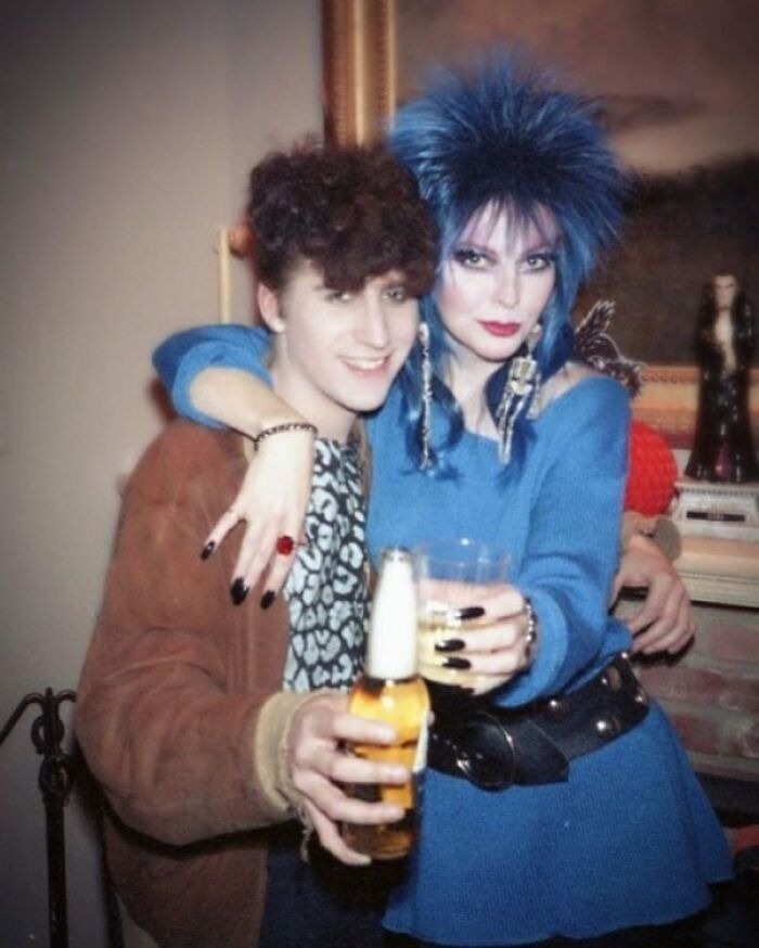 Two people posing with drinks showcasing iconic 80s hairdos, including voluminous blue teased hair and curly styles.
