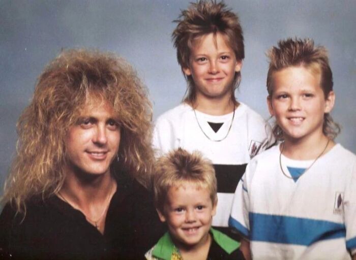 Group photo of four people sporting iconic 80s hairdos including big, spiked, and mullet styles typical of the decade.