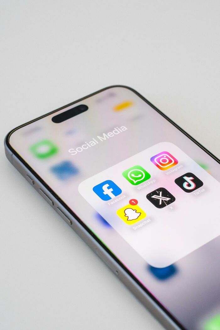 Smartphone screen showing social media apps like Facebook, WhatsApp, Instagram, X, Snapchat, and TikTok icons.