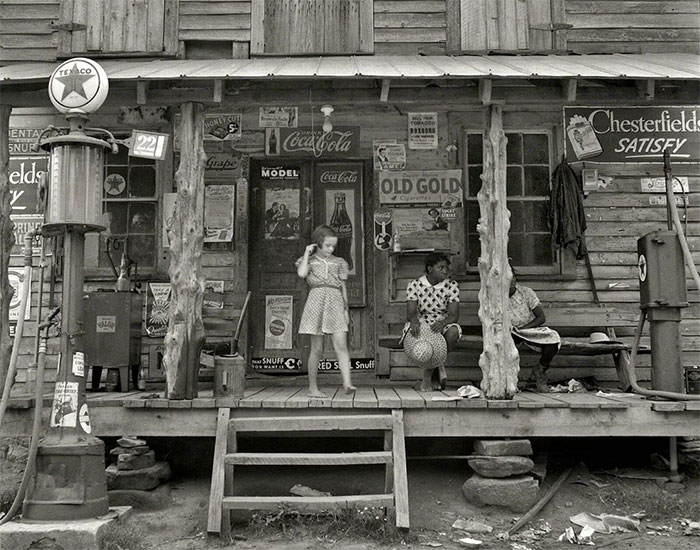 Black and white photo of children on the porch of an old wooden store, showing a side of history rarely seen in textbooks.