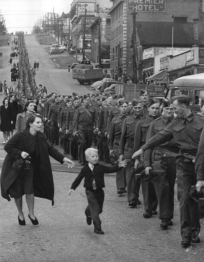 Black and white photo of soldiers marching in a parade as a young boy reaches out to greet them historical pics unseen in textbooks