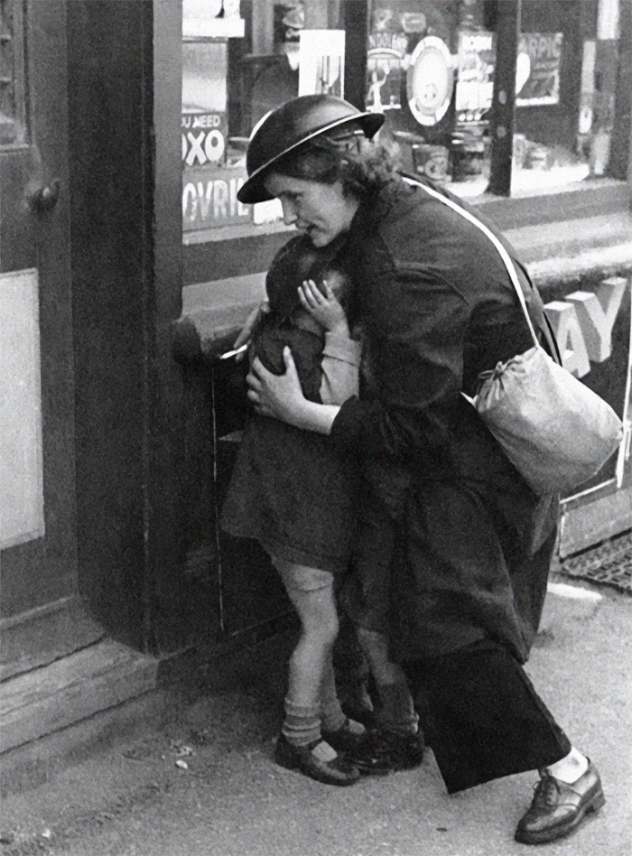 Black and white photo showing a woman in a helmet comforting two children, capturing a rare side of history image.