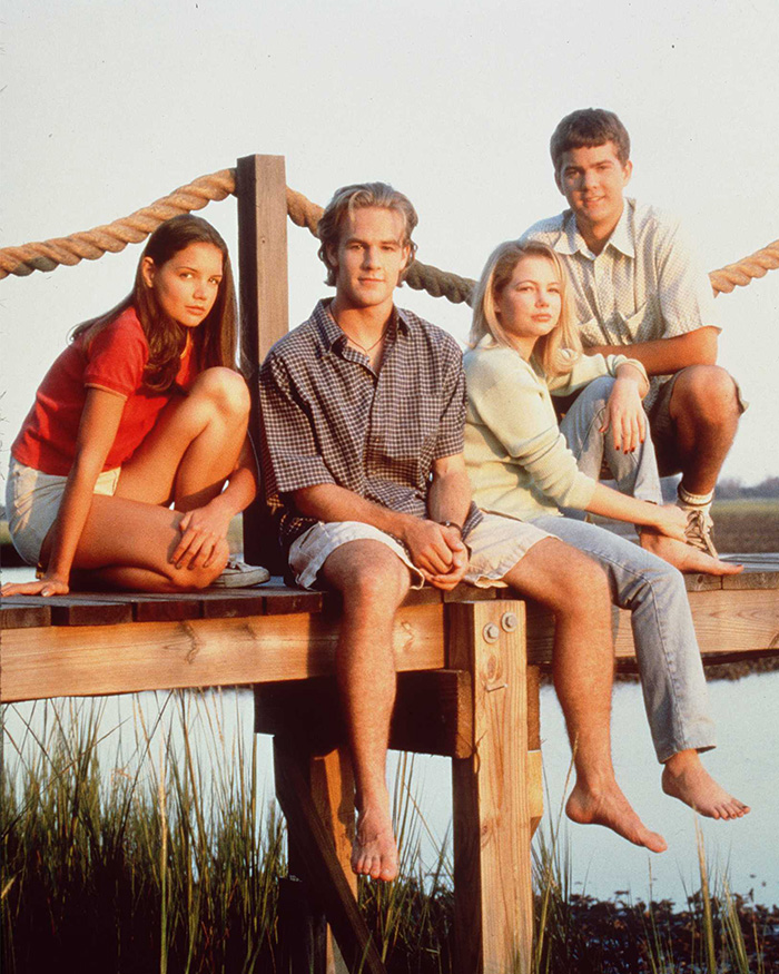 Four young actors from Dawson's Creek sitting on a wooden dock by the water during sunset, including James Van Der Beek.