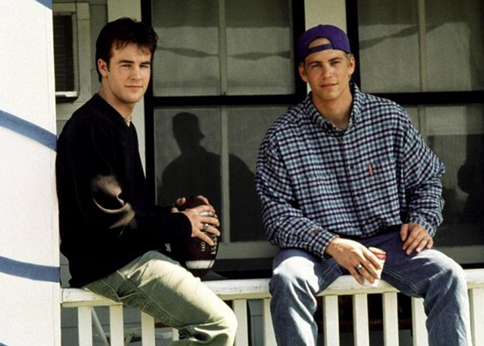 Two young men sitting on a porch railing, one holding a football and the other a cup, representing James Van Der Beek Dawson's Creek.