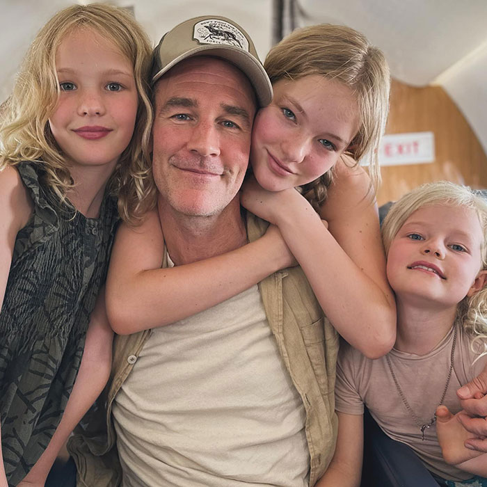 James Van Der Beek smiling with three children hugging him inside a cozy setting, capturing a tender family moment.