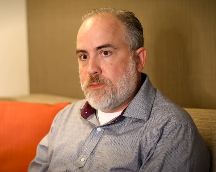 Middle-aged man with beard sitting on a couch, appearing thoughtful while discussing Elon Musk&rsquo;s daughter and UFO files.