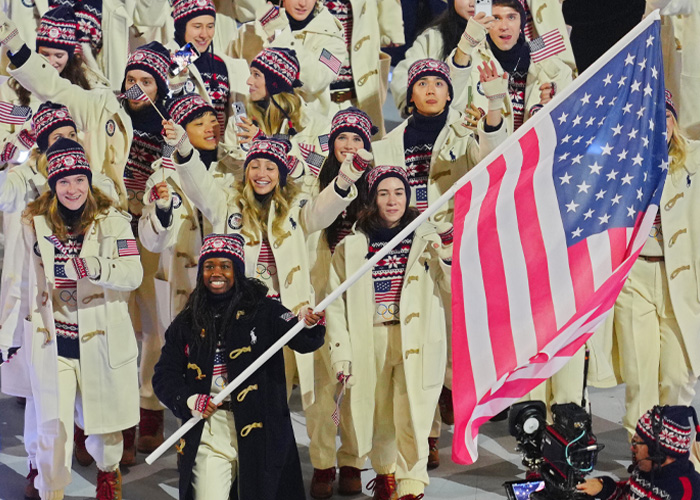 US athletes marching at Winter Olympics inauguration ceremony, wearing team uniforms and waving American flags.