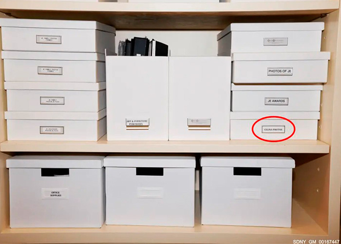 Shelves filled with white storage boxes labeled with photos and documents related to Epstein obsession files.