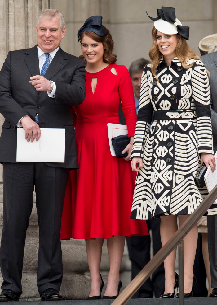 Prince Andrew with Princess Beatrice in red dress and Princess Eugenie in patterned coat at a formal royal event.