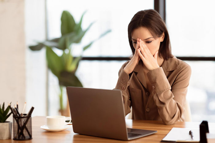 Woman at desk looking stressed during remote meeting, dealing with coworker preaching about Jesus and holy drama at work.