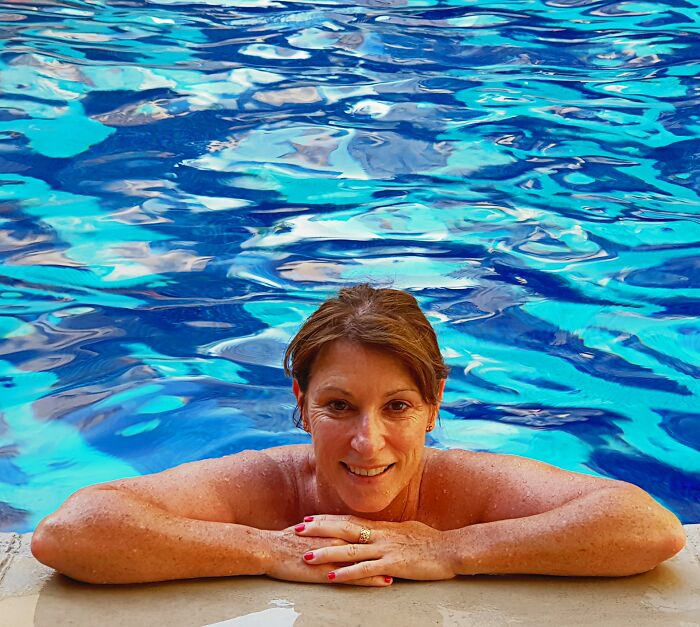 Woman smiling while resting at the edge of a swimming pool, symbolizing unexpected friendship endings stories.
