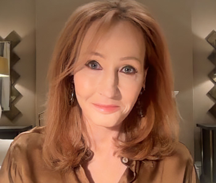 J.K. Rowling with red hair, wearing brown top and earrings, sitting indoors in a softly lit room discussing Epstein accusations.