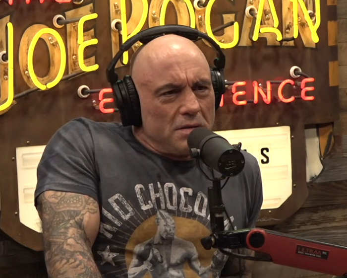 Joe Rogan speaking into a microphone wearing headphones during a podcast recording session.