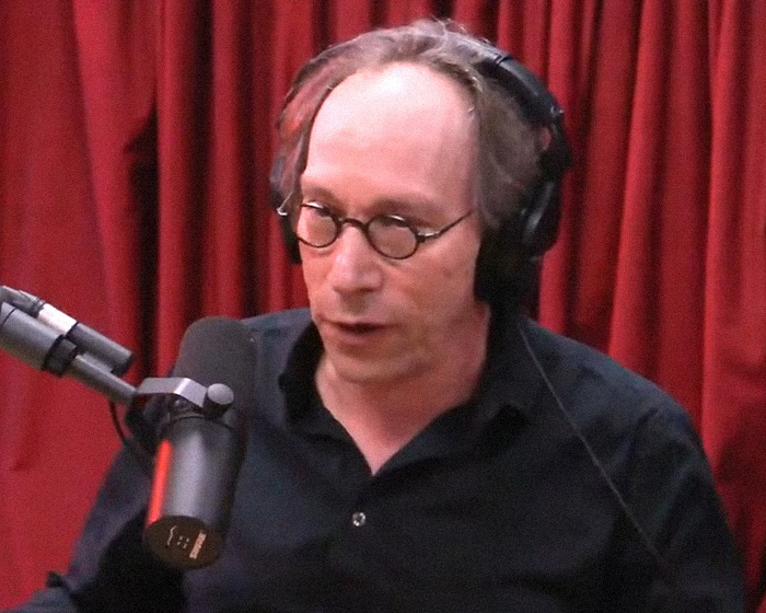 Podcaster wearing headphones and glasses speaking into a microphone in a studio, related to Joe Rogan Epstein files discussion.
