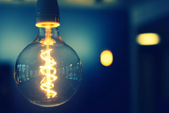 Glowing vintage light bulb with spiral filament in a dark room, evoking strange things people witnessed questioning everything.