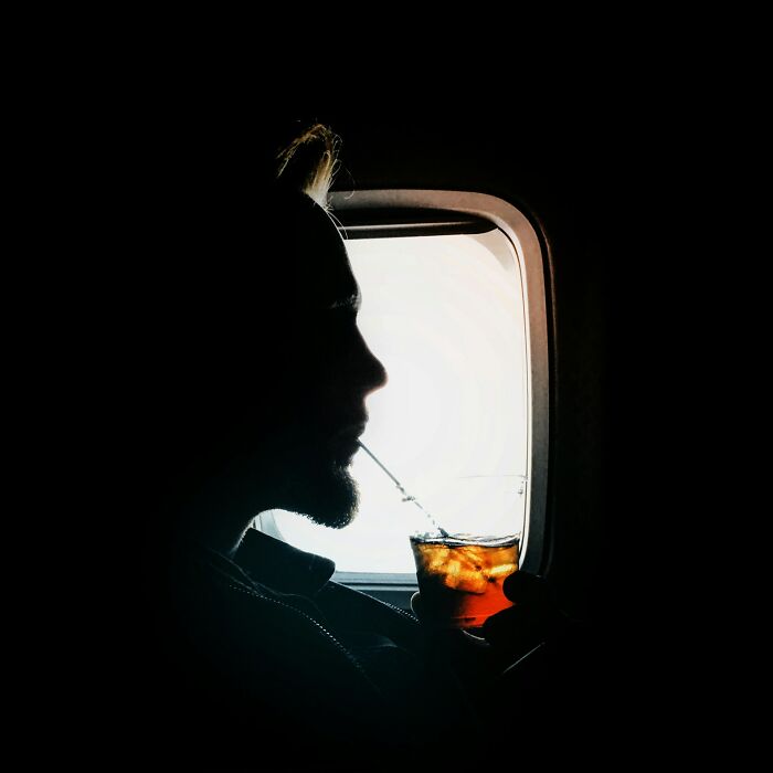 Passenger enjoying a drink by the airplane window, highlighting underrated plane perks to enhance travel experience.