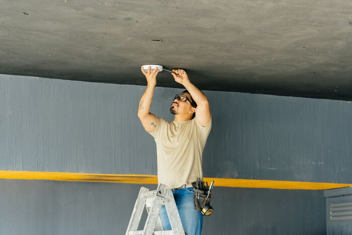 Man on ladder installing a ceiling device, highlighting chilling sounds that signal immediate disaster awareness and safety.