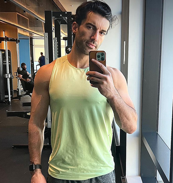 Man taking a gym mirror selfie wearing a sleeveless shirt, highlighting awkward fashion faux pas in court showdown context.