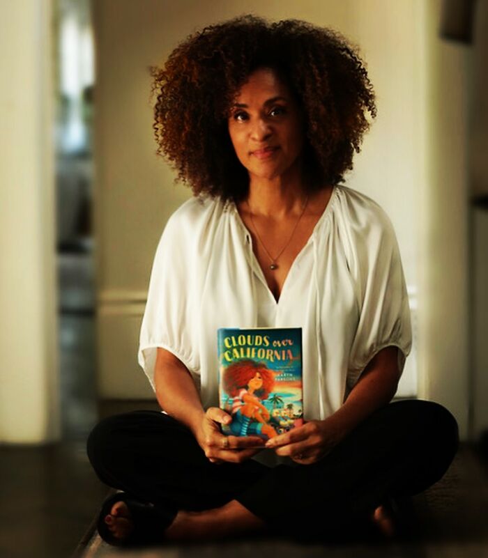 Woman with curly hair sitting cross-legged indoors holding a book, representing iconic actors who dominated Hollywood.