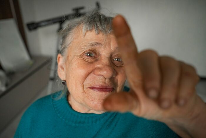 Elderly woman in teal sweater pointing at camera, evoking eerie feeling related to graveyard shift workers’ strange encounters.