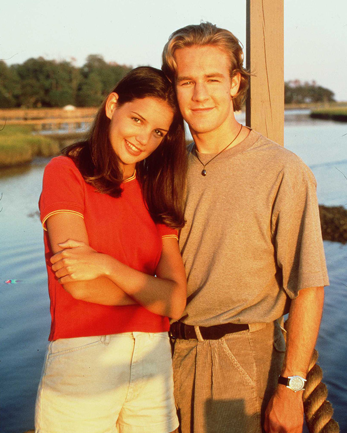 Katie Holmes and James Van Der Beek smiling together outdoors by the water in a nostalgic portrait.