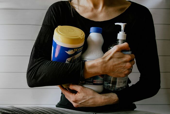 Person holding household cleaning products close to their chest, highlighting dangerous things often dismissed.
